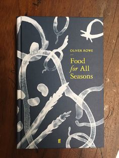 a book on food for all seasons sitting on a wooden table next to a knife and fork