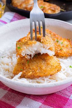 two pieces of fried fish on top of rice with a fork in the bowl next to it