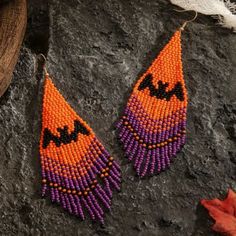 two orange and purple beaded earrings sitting on top of a rock next to a leaf