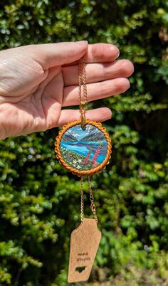 a person holding up a small necklace with a mountain scene in the center and trees behind it