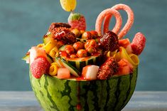 a watermelon bowl filled with lots of different types of food and candy sticks sticking out of it