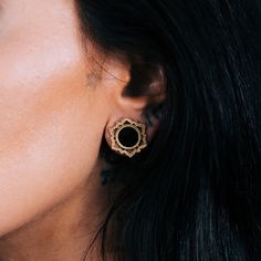 a close up of a woman's face wearing gold earring with an intricate design