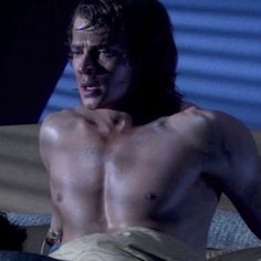 a shirtless man sitting on top of a bed next to a blue wall in the dark