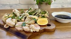 a wooden cutting board topped with food next to a bowl of dipping sauce