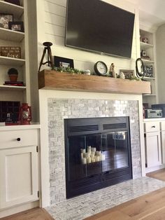 a television mounted above a fireplace in a living room with white cabinets and wood flooring