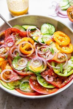 a bowl filled with sliced up vegetables on top of a table next to a glass of orange juice