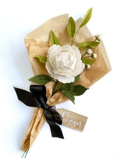 a bouquet of flowers is wrapped in brown paper and tied with a black ribbon that says mom