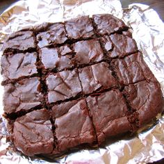 a close up of a piece of brownie on tin foil with one cut in half