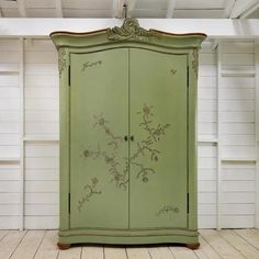 a green armoire in a room with white walls and wood flooring, decorated with floral designs