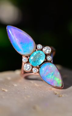 Australian Opal and Paraiba Tourmaline Trinity Talisman Ring in solid 14k Rose Gold with Diamonds. 35mm in length This amazing Lemurian Trinity Ring features a very special Paraiba tourmaline paired with pink and purple opals with matching neon blue fire in rose gold with diamond accents! This piece is truly enchanting, with a magnificent combination of stones and a fierce yet elegant design that perfectly embodies an earthy yet majestic feel. Opal ignites the energy body with a full spectrum pr Talisman Ring, Radiant Rings, Jewelry Sketches, Alchemy Jewelry, Australian Opal Jewelry, Lavender Opal, Mid July, Trinity Ring, Earthy Jewelry