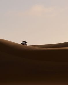 a car is driving through the desert with sand dunes in the foreground and clouds in the background