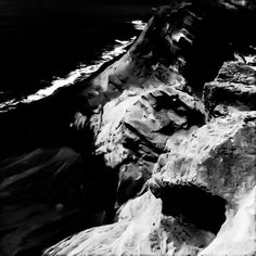 black and white photograph of rocks on the side of a mountain with water in the background