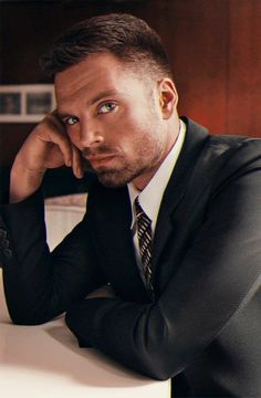 a man in a suit sitting at a table with his hand on his chin and looking off to the side