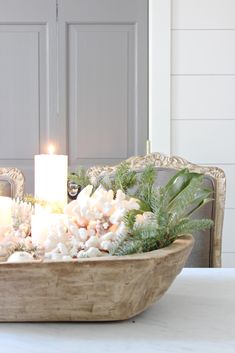 a wooden bowl filled with white flowers and candles on top of a table next to a door