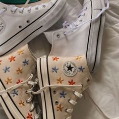 two pairs of white converse sneakers with colorful flowers on the soles are laying on a bed