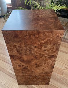 a wooden box sitting on top of a hard wood floor next to a potted plant