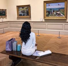 a woman is sitting on a bench in an art gallery looking at paintings and books