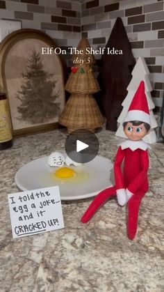 an elf is sitting on the counter next to a plate with an egg in it