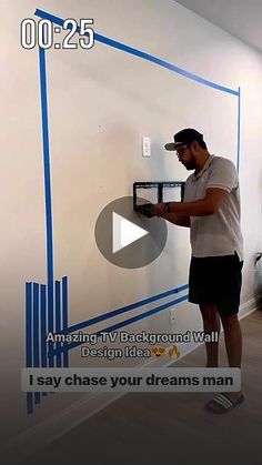 a man standing in front of a white wall with blue tape on it and writing on the wall