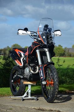 an orange and black dirt bike parked on top of a wooden bench in the grass