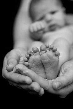 a black and white photo of a baby's feet being held by two hands