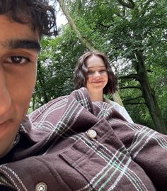 a man and woman standing next to each other in the woods