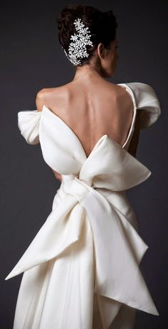 the back of a woman's white dress with a large bow on her shoulder