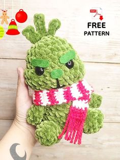 a hand holding a green stuffed animal with a scarf around it's neck and eyes