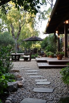 A serene backyard with a gravel path, patio seating, and lush greenery. Backyard Accent Wall, Backyard No Grass Landscaping, Backyard Zones Outdoor Living, Dg Backyard Landscape Design, Backyard Landscape Ideas On A Budget, Simple Yard Landscape, Diy Backyard Landscape Ideas On A Budget, Rock Backyard Ideas, California Backyard Ideas