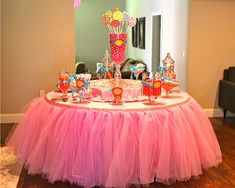 a pink tulle skirted table with candy and lollipops on it