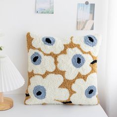 a white pillow with blue and brown flowers on it sitting on a table next to a lamp