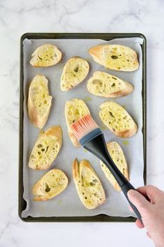 a person holding a brush over some bread on a baking sheet with other pastries