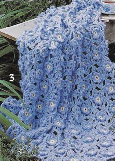 a blue crocheted blanket sitting on top of a wooden bench next to plants