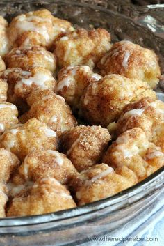 a glass bowl filled with cinnamon rolls covered in icing on top of a table