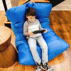 a young boy sitting on a blue bean bag chair with a tablet in his lap