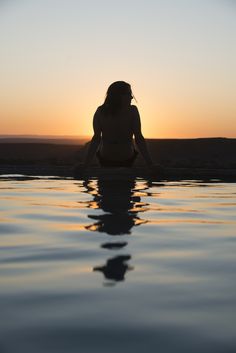 a woman is sitting in the water at sunset