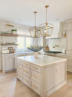 a large kitchen with white cabinets and gold accents on the island countertop, along with two pendant lights hanging from the ceiling