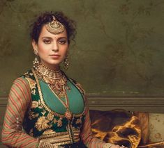 a woman in a green and gold outfit sitting on a couch with her hands clasped