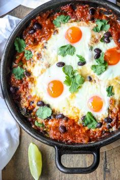 an iron skillet filled with eggs, black beans and cilantro on top of a wooden table