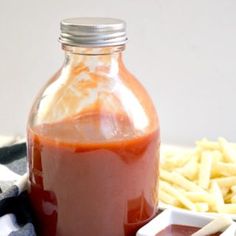 homemade ketchup in a glass bottle next to french fries and a bowl of dipping sauce