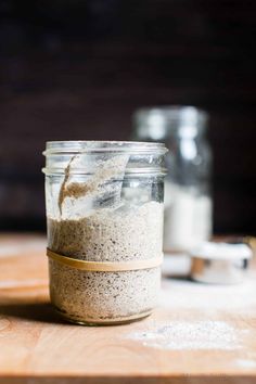 a glass jar filled with food sitting on top of a wooden table next to two salt shakers