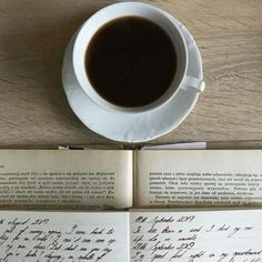 an open book next to a cup of coffee on top of a wooden table with writing