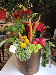 a metal bucket filled with lots of different types of flowers and vegetables on top of a table