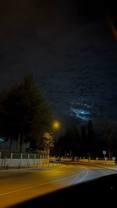 an empty street at night with the lights on and dark clouds in the sky above