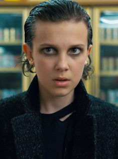 a woman with dark hair and blue eyes looks at the camera while standing in front of bookshelves