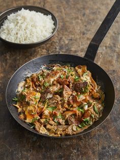 a skillet with rice and meat in it next to a spoon on a table