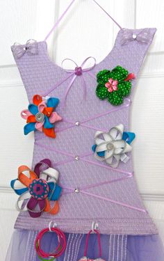 a purple dress hanging on the wall with colorful hair clips and flowers attached to it