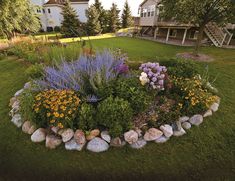 a garden with rocks and flowers in the center, surrounded by green grass near a house