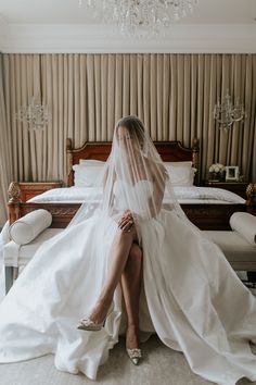 a woman sitting on top of a bed wearing a white dress and veil over her head