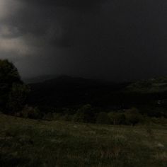 the sky is dark and cloudy over some hills